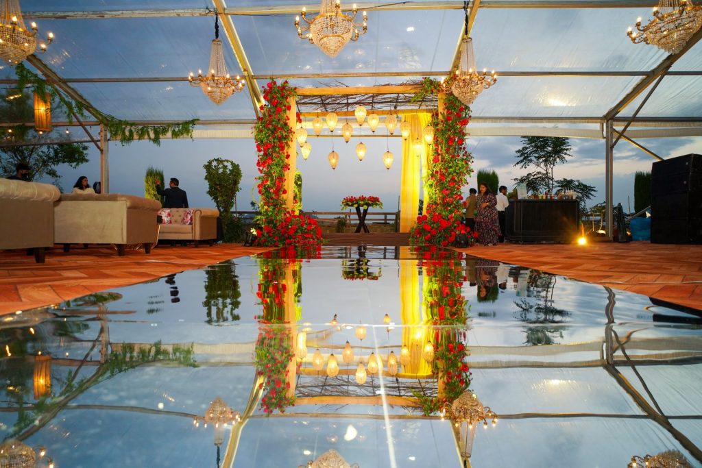 Chic indoor event setup with chandeliers, floral decor, and mirrored reflections during dusk.