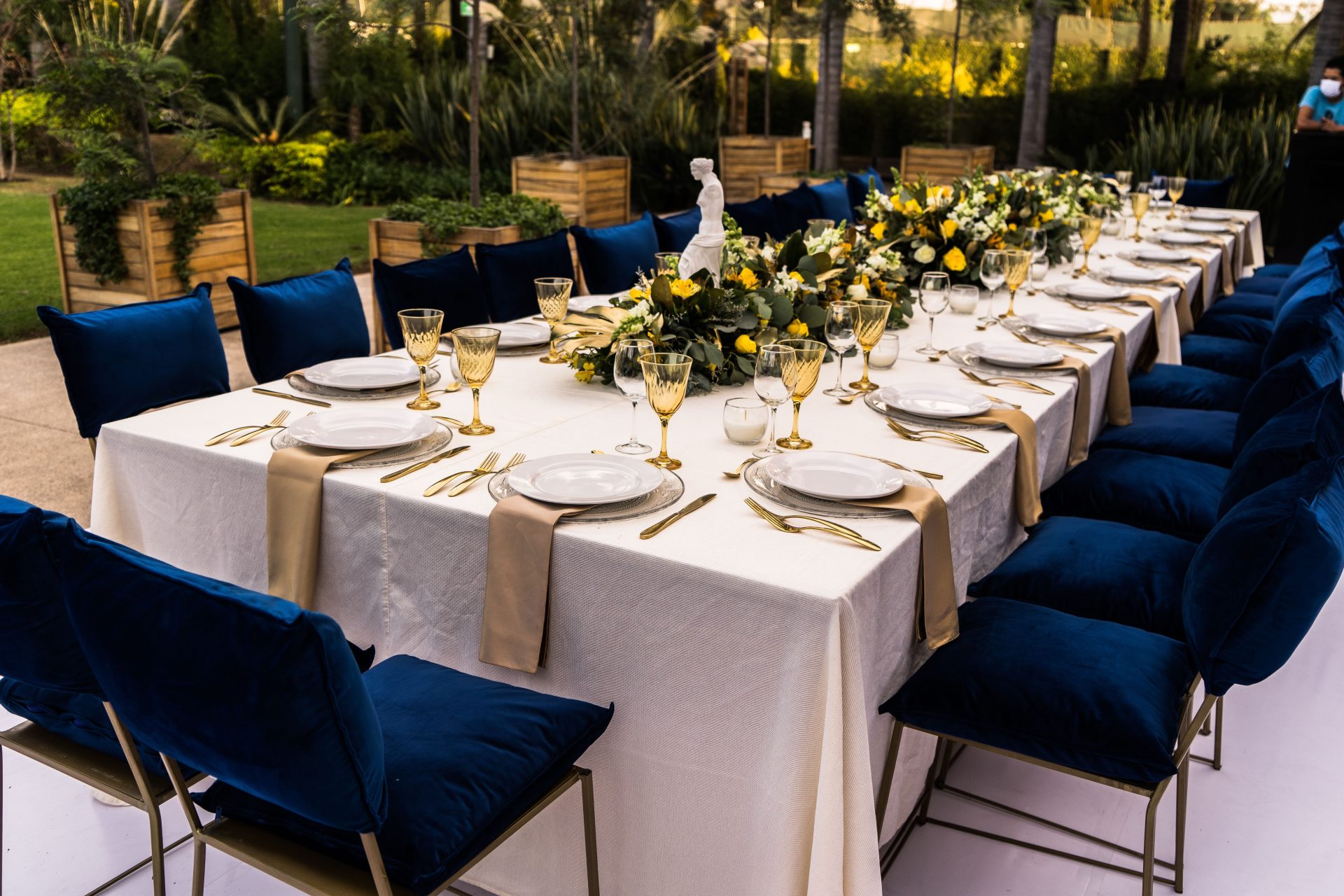 A beautifully decorated table set outdoors for a sophisticated celebration with floral arrangements and blue accents.