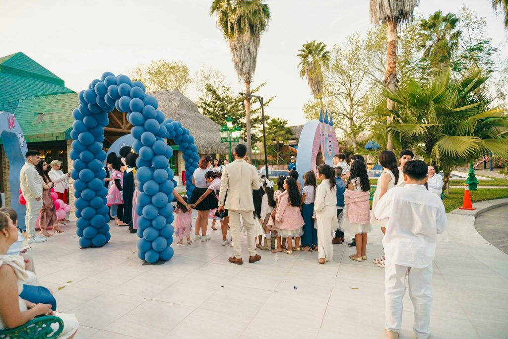 People gather under a blue balloon archway outdoors